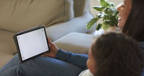 Mother and child using tablet on couch holding blank-screen device for app mockups