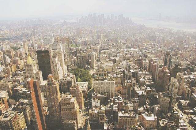 This aerial view captures the dense collection of skyscrapers and buildings on a hazy day in New York City. Ideal for use in travel blogs, tourism advertisements, urban planning presentations, and articles showcasing city landscapes and architecture. The image conveys the busy, vibrant life of the metropolis.