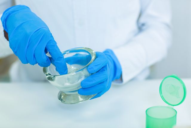 Pharmacist wearing blue gloves grinding medicine in a mortar and pestle. Ideal for illustrating pharmaceutical compounding, healthcare practices, and medical preparations. Useful for articles, educational materials, and healthcare-related content.