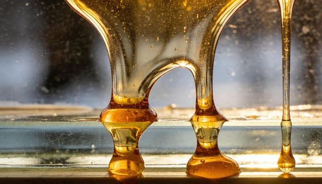 Backlit golden honey droplets clinging to glass window macro glossy viscous texture