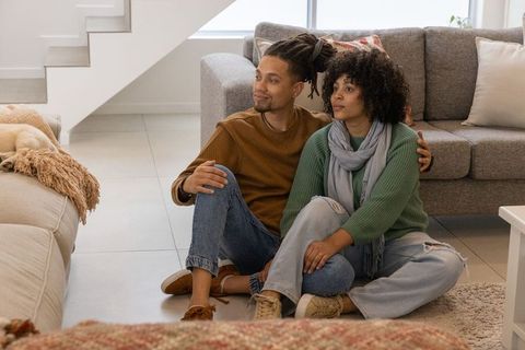 African american couple sitting on floor leaning on sofa sharing moment in modern home