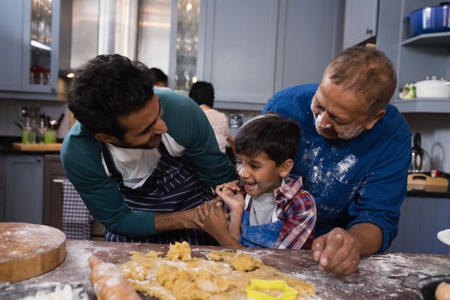 Multi-generational family happily baking together in a modern kitchen. Grandfather, father, and child engaging in fun cooking activity with dough and cookie cutters. Great for use in family bonding, culinary arts, and lifestyle content.