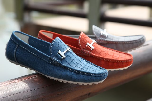 Three pairs of colorful leather loafers displayed on wooden bench in natural light. Perfect image for fashion catalogs, shopping websites, shoe store advertisements, and lifestyle blogs. Ideal for content related to men's fashion, footwear trends, and casual footwear.