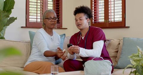 Caregiver Assisting Senior Woman with Glucometer at Home