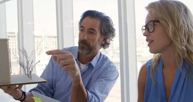 Two architects discussing building project using a model at modern office. Suitable for depicting teamwork, collaboration in design firms, architectural review meetings, and project planning phases in business settings.