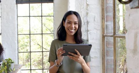 Smiling woman using tablet in bright modern workspace