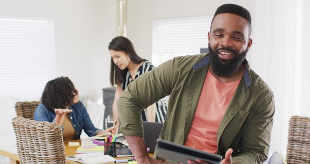 Happy african american man using tablet, working with diverse female friends, in slow motion. Friendship, working from home, small business and start up business concept.