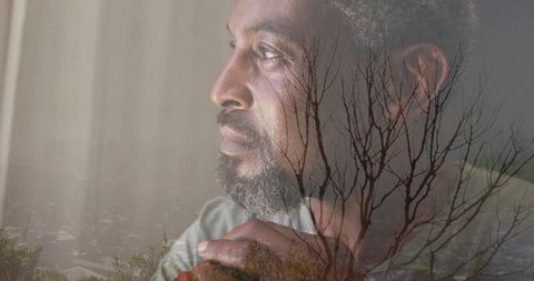 Gazing mature man clasping hands, double exposure branches and misty shoreline contemplation