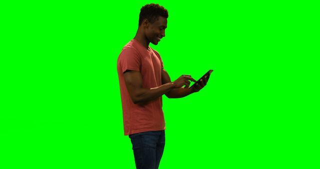 Young man in casual clothing using a tablet against a green screen background. Suitable for promotional materials, technology advertisements, user interface demonstrations, and software tutorials. Potential use in digital media, e-learning applications, and virtual presentations where green screen allows for background customization.