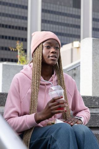 African american woman sipping iced drink urban plaza steps wearing pink hoodie and beanie