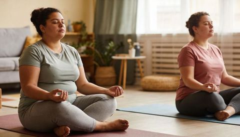 Two women meditating in cozy living room on yoga mats practicing mindfulness and calm