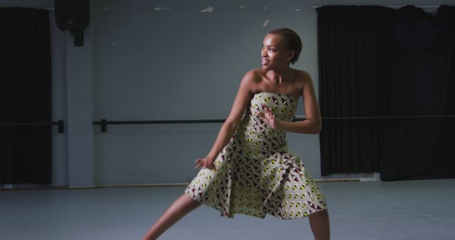 Young woman performing an energetic contemporary dance routine in a studio, wearing a patterned dress. Ideal for use in articles and promotions related to dance, performing arts, fitness activities, artistic expressions, and creative movements.
