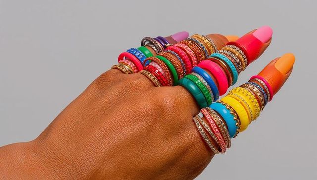Stacking neon and gemstone rings on brown-skinned female hand with colorful manicure