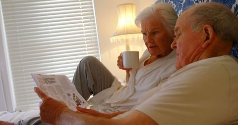 Senior Couple Relaxing in Bedroom Drinking Coffee and Reading Newspaper