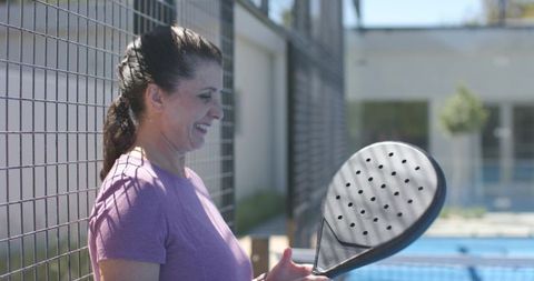 Mature woman smiling holding padel racket on sunny outdoor padel court showing confidence