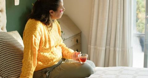 Woman Relaxing with Tea in Bright Sunlit Bedroom