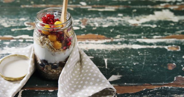 A jar of yogurt parfait with layers of fruits, granola, and nuts sits on a rustic wooden table, with copy space. Healthy eating habits are exemplified by this nutritious and visually appealing snack option.