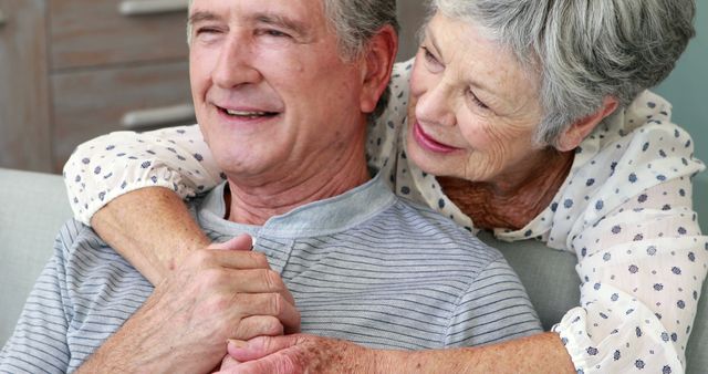 Elderly couple sharing a warm embrace at home. The couple is smiling and expressing their love and affection. Ideal for use in content related to aging, relationships, family bonds, elderly care, and retirement. Great for brochures, websites, and advertisements focusing on senior citizens and their quality of life.