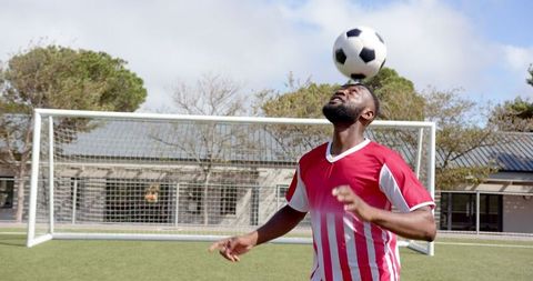 Athletic african american man balancing soccer ball on forehead amidst game