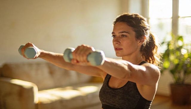 Focused woman lifting light dumbbells in sunlit living room for at-home strength workout