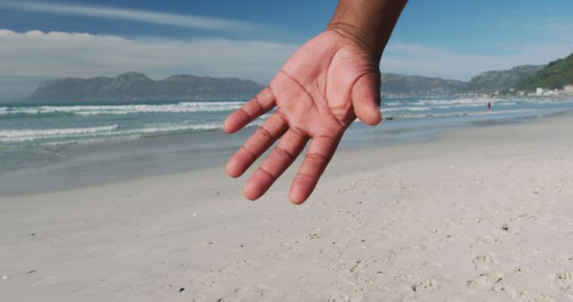 Open hand reaching out with sandy beach and gentle waves in the background. Perfect for concepts of connection, relaxation, inviting nature, peaceful vacation moments, or promotion of travel destinations.