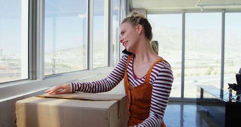 Businesswoman communicating and carrying box in modern office