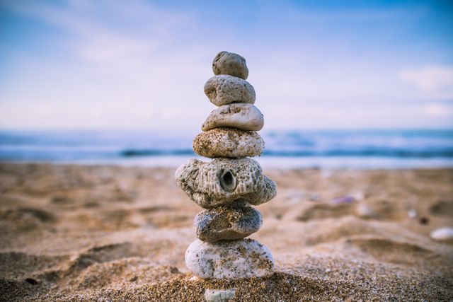 Stack of rocks balancing on sandy beach near ocean shoreline. Great for illustrating concepts of balance, mindfulness, and tranquility. Perfect for wellness, meditation, and nature-related content.