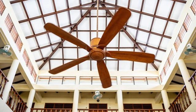 Wooden five-blade ceiling fan rotating in vaulted atrium with timber trusses and louvers