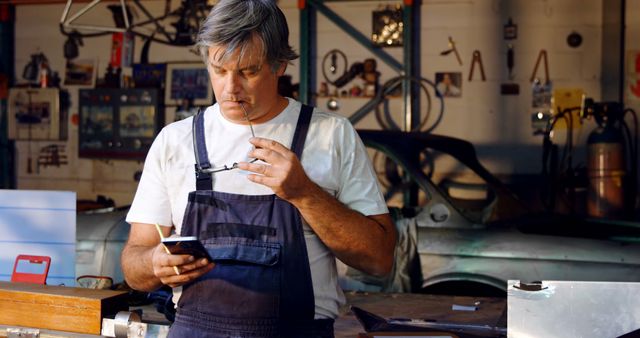 Senior Man in Workshop Reading Smartphone with Glasses - Download Free Stock Images Pikwizard.com