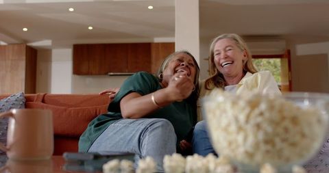 Diverse Women Enjoying Laughter and Popcorn in Modern Living Room