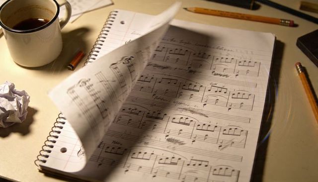Composing late night piano manuscript in spiral notebook with coffee, pencils, eraser