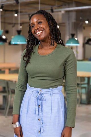 African american woman smiling in modern coworking cafe wearing olive top and blue skirt
