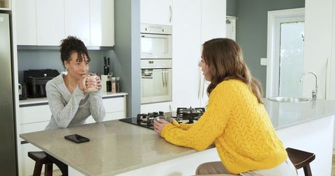 Diverse friends chatting at modern kitchen island holding mugs and enjoying morning coffee