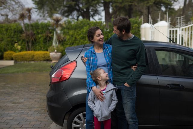 Family standing together near a car outdoors, smiling and bonding. Ideal for use in advertisements, family-oriented content, lifestyle blogs, and parenting articles.
