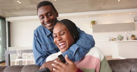 Joyful Couple Sharing Laughter at Home Using Smartphone