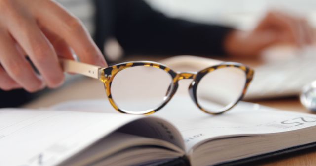 Close-Up of Hand Placing Glasses on Open Book in Office - Download Free Stock Images Pikwizard.com