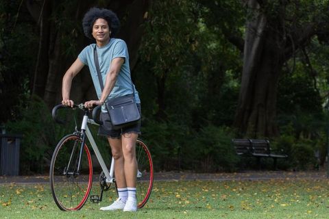 African american man standing with fixie bicycle in park wearing messenger bag and sneakers