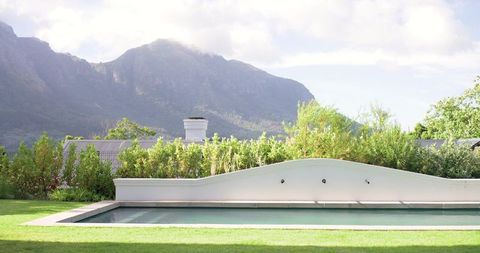 Sunlit backyard pool with curved white wall, hedge border and mountain backdrop