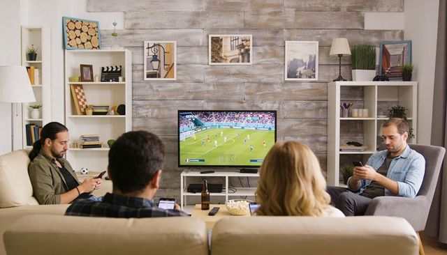 Friends watching soccer match in cozy rustic living room with popcorn, beer, smartphones