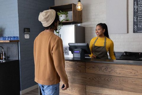 Cashier accepting smartphone payment at rustic cafe counter with qr code touchscreen