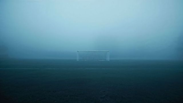 Lonely soccer goal fading into dense fog on empty pitch minimal eerie sports solitude