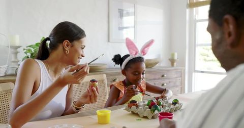 Family Decorating Easter Eggs Together at Dining Table