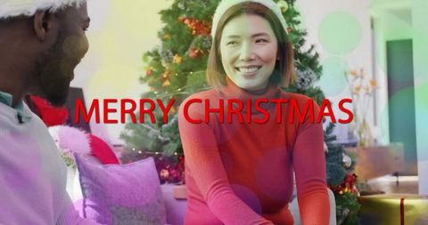Couple sharing cozy christmas moment by decorated tree with merry christmas text