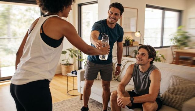 Friends sharing reusable water bottle after home workout smiling healthy hydration casual