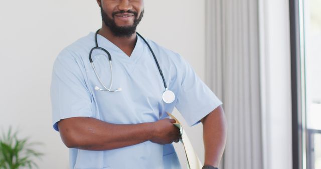 Confident African American male nurse holding a file and wearing a stethoscope. He is smiling and appears professional. Ideal for use in medical, healthcare, and nursing advertisements or articles, illustrating the professionalism and approachability of healthcare workers.