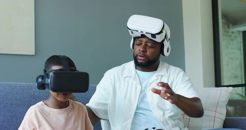 African father and son playing with VR headsets on couch exploring virtual worlds together