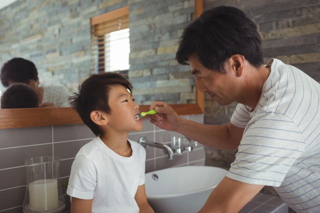 Father brushing his son's teeth in a modern bathroom. Ideal for use in articles or advertisements about family life, parenting tips, dental hygiene, morning routines, and father-son bonding moments.