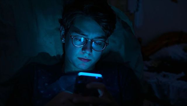 Teenager relaxing with smartphone in dark bedroom at night