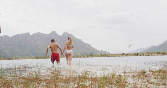 Caucasian couple walking in lake water and holding hands with copy space. Nature, travel, tranquility, lifestyle concept, unaltered.