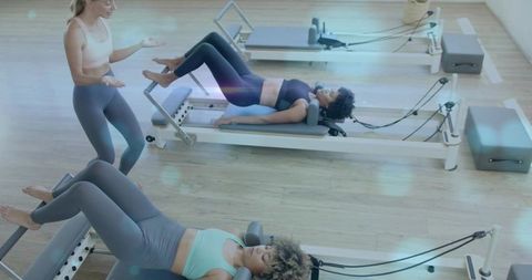 Instructor guiding women on pilates reformers performing leg presses in bright studio